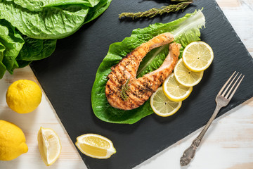 Salmon fillet. Grilled salmon with herb and lemon on black slate board. Fish roasted on a wooden background.