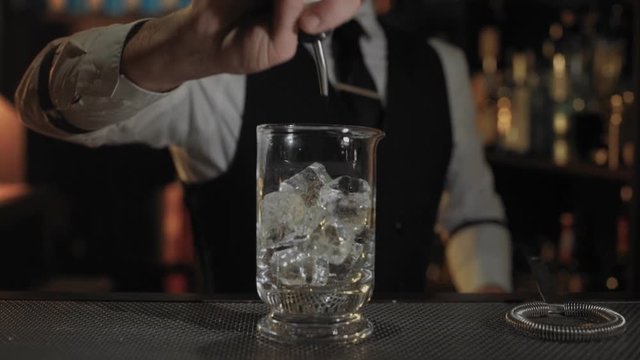 Camera moves toward unrecognizable bartender that is pouring rose vermouth to big vase with ice to cool it before serving. Demonstration bar lifestyle and art of cocktail making business concept