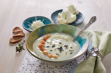 Creamy cauliflower soup in a blue cup with croutons, thyme and and parmesan cheese on wood
