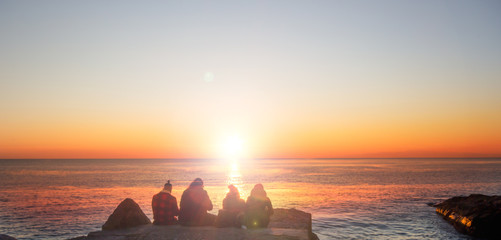 Naklejka na ściany i meble Group of friends see the Scenic view of beautiful sunset above the sea in natural background.