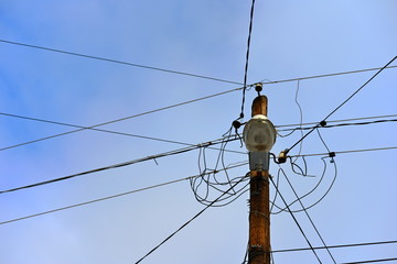 Wooden electric pole with wires on the street in the city against a blue sky.