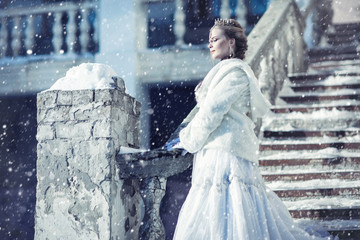 A girl in a white fur coat and crown against the background of an old building