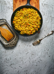 top view of a risotto with vegetables and vegan beet cutlets served on a black cast-iron frying pan on a gray concrete backdrop. also in the frame an old fork and a wooden kitchen spatula on a vintage