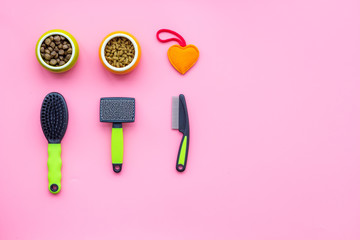 Grooming equipment for pets near bowls with animal feed on pink bakground top view copy space