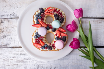 Cake in shape of number 8 decorated with berries and flowers tulips. Dessert for women's day on the eighth of March