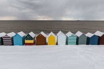 Row of beach huts in winter snow on coast of Herne Bay, Kent, England