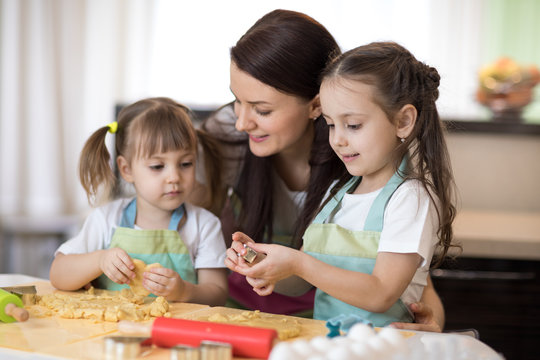 Mom with her 2 and 5 years old daughters are cooking in domestic kitchen to Mothers day