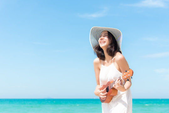 Summer Vacation. Smelling asian women relaxing and playing an ukulele on the beach, so happy and luxury in holiday summer, blue sky background. Travel and lifestyle Concept.