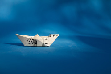 Paper boat made of musical score sheet in blue background