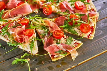 Italian pizza with ham, tomatoes, cheese and herbs on vintage wooden background.