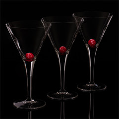 Three empty martini glasses on a black reflective surface. There is a red cherry in each glass