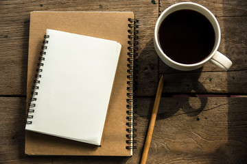 Top view of blank notebook with white coffee, laptop and with natural light on wooden table.