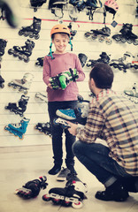 Male shop assistant helping boy to try on roller-skates