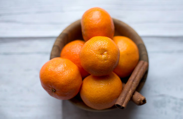 Ceramic bowl with ripe mandarin citrus and cinnamon sticks on wooden table, close-up