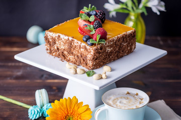 Homemade square cake decorated with yellow jelly on top and berries with mint on dark background