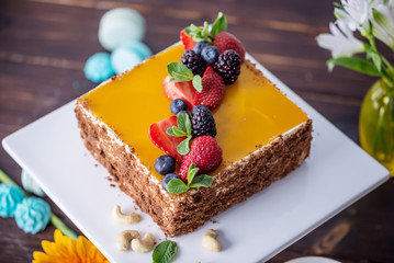 Homemade square cake decorated with yellow jelly on top and berries with mint on dark background