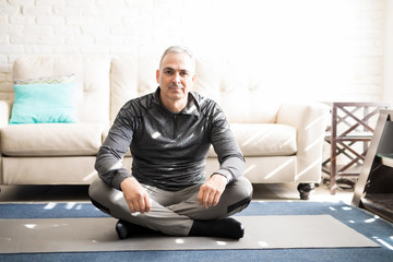 Fototapeta premium Relaxed mature man sitting on yoga mat at home