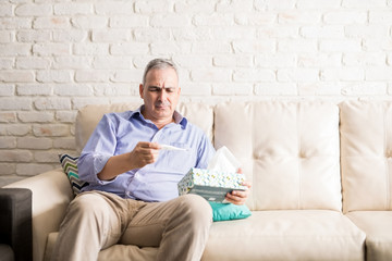 Fototapeta premium Sick man measuring his fever with thermometer