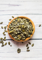 Bowl with raw pumpkin seeds on wooden background