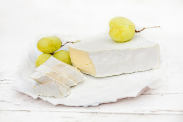 Fresh Brie cheese with slices and grape on white rustic on a wooden board. Brie type of cheese. ...