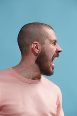 Obraz premium The young emotional angry man screaming on blue studio background