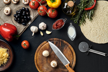 Cutting wooden board with traditional pizza preparation ingredients: cheese, tomatoes sauce, mushrooms, olive oil, pepper, spices. Black texture table background