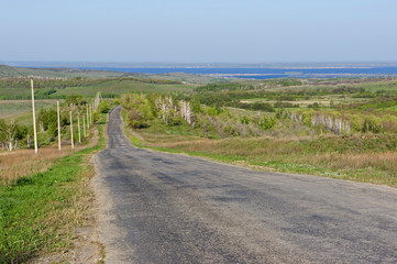 Fototapeta premium The road leads through the hills to a large river. The first spring greens and the blue sky. View from the hills to the Volga River.