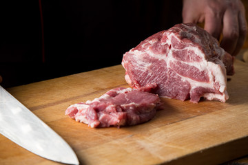 Cook cuts  fresh piece of meat on a wooden cutting board