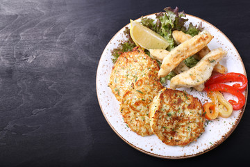 Fried fish with zuccini pancakes and fresh vegetables. Top view