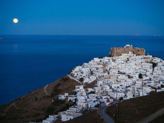 A lithe road leading to Chora of Astypalaia in blue hour and the full moon rising from the horizon