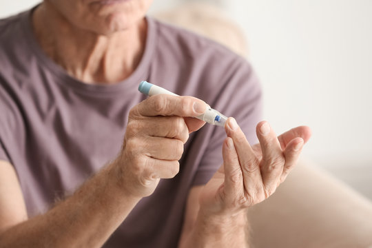 Elderly man with diabetes measuring level of blood sugar at home, closeup
