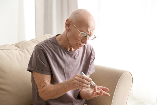 Elderly man with diabetes measuring level of blood sugar at home