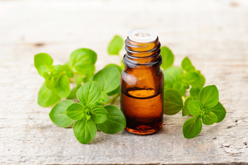 Oregano essential oil and fresh oregano leaves on the wooden board