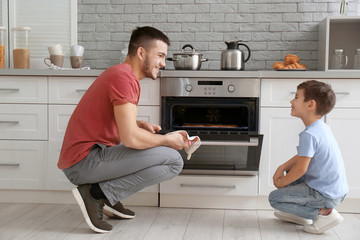 Little boy watching his father bake cookies in oven indoors