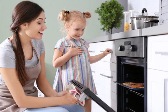 Little girl watching her mother bake cookies in oven indoors