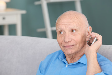 Senior man with hearing aid talking on phone indoors