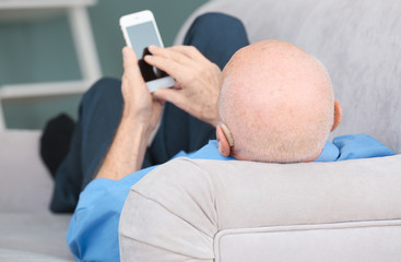 Senior man with hearing aid using smartphone indoors