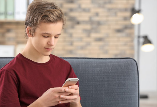 Teenage boy with hearing aid using smartphone indoors