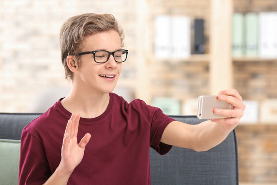 Teenage boy with hearing aid using smartphone indoors