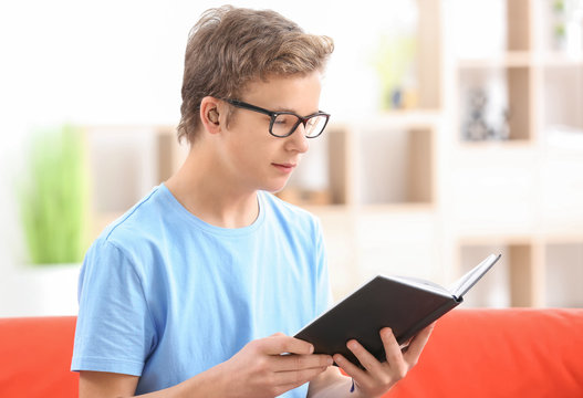 Teenage boy with hearing aid reading book indoors