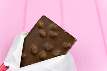 A  chocolate bar with nuts on a pink background.
