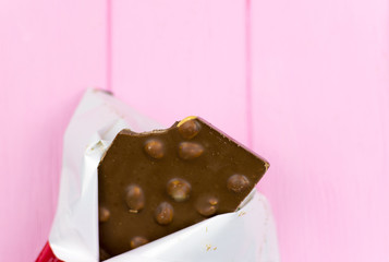 A bitten chocolate bar with nuts on a pink background.