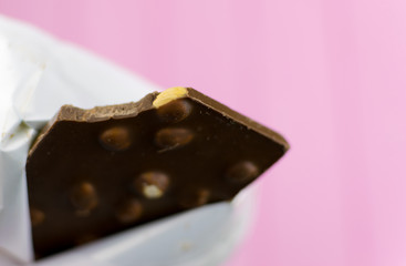 A bitten chocolate bar with nuts on a pink background.