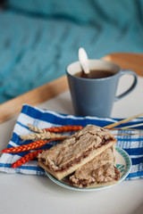 A vertical image of homemade pastries on a small plate, a blue cup of tea, a spoon, a blue and white striped towel and spikelets. Served on a white tray. Selective focus.