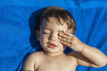 Little boy with closed eyes lie down in a blue towel.