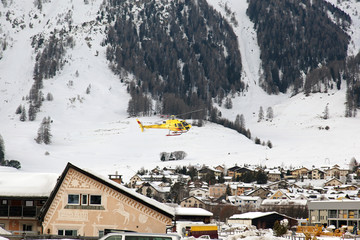 A yellow sightseeing tour helicopter flying over the cute village in the alps switzerland in winter