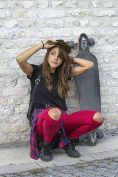 Young urban girl kneel in front of brick wall with skateboard beside her