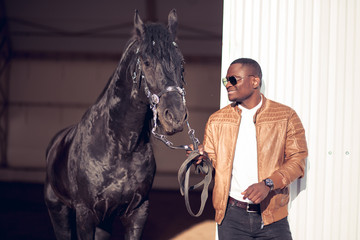 african Man wearing sunglasses near a black horse in hangar