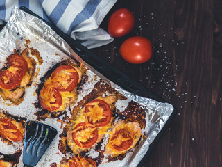 Chicken fillet baked with tomatoes and cheese on a baking sheet with foil. Delicious healthy food. Lifestyle. Flat lay. Top view. Wooden background
