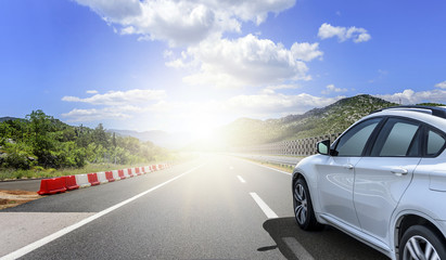 Obraz na płótnie Canvas A white car rushing along a high-speed highway in the sun.